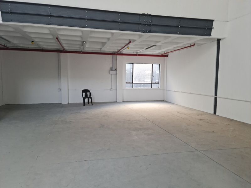 Spacious industrial utility area featuring exposed steel beams, concrete waffle ceiling, fire sprinkler system, and polished concrete flooring with natural light.