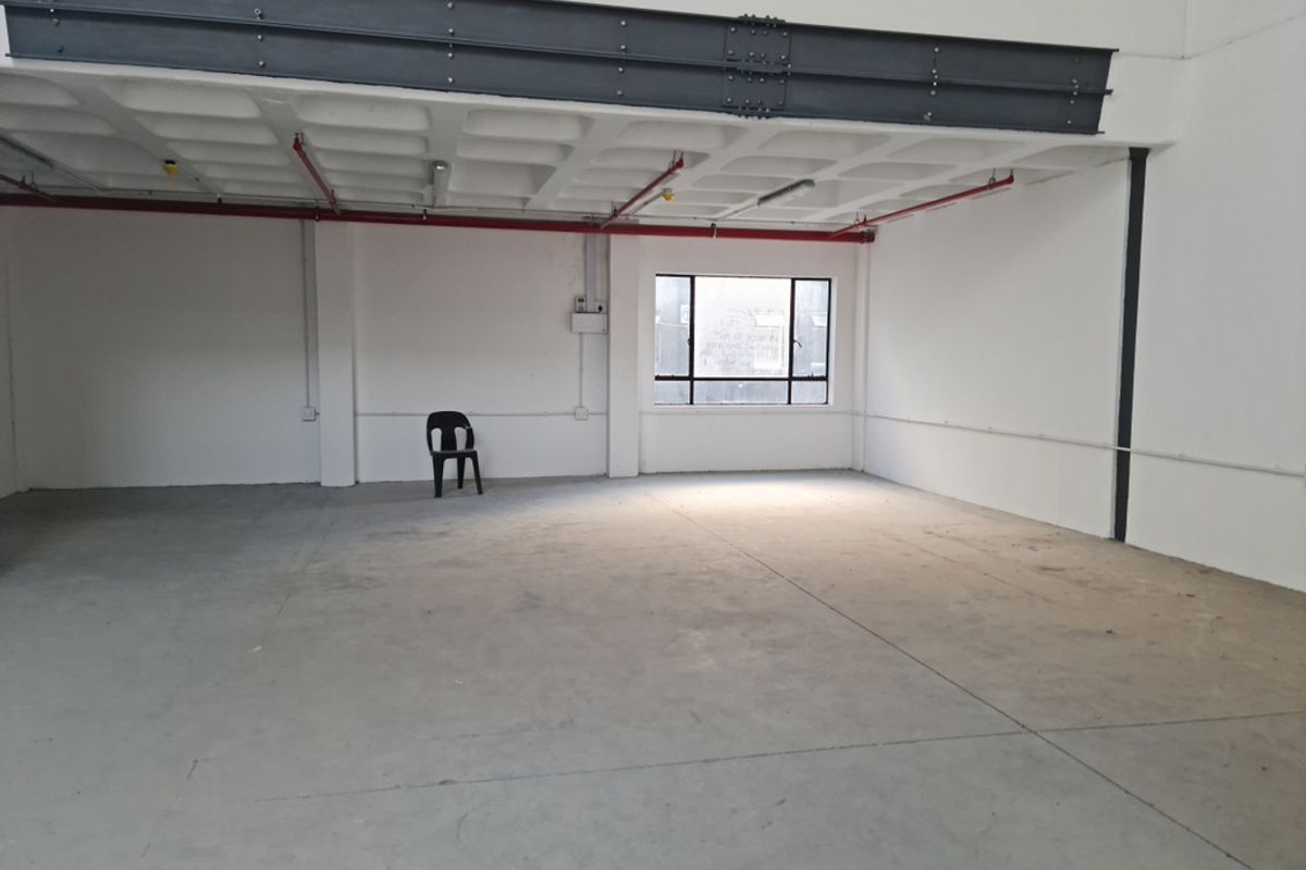 Spacious industrial utility area featuring exposed steel beams, concrete waffle ceiling, fire sprinkler system, and polished concrete flooring with natural light.
