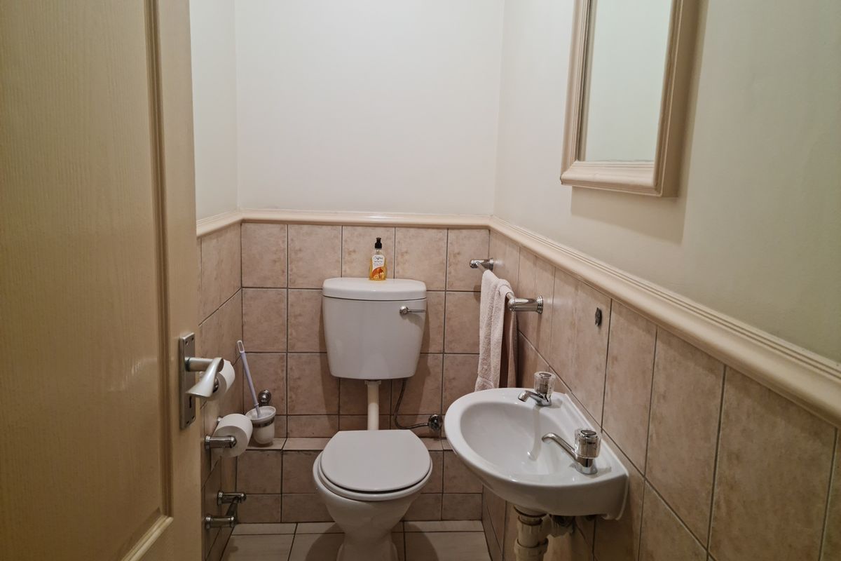 A compact guest bathroom featuring a standard toilet, wall-mounted basin, and neutral tiled finishes.