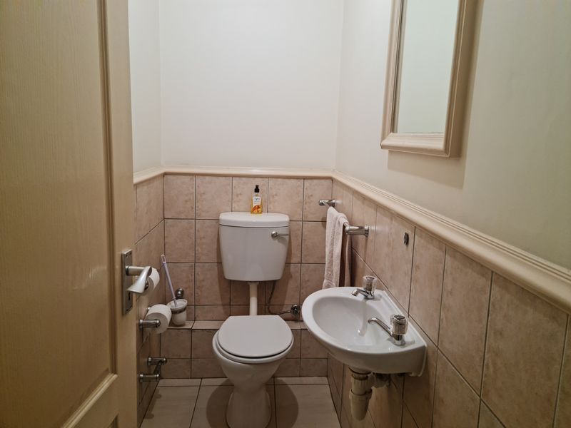 A compact guest bathroom featuring a standard toilet, wall-mounted basin, and neutral tiled finishes.