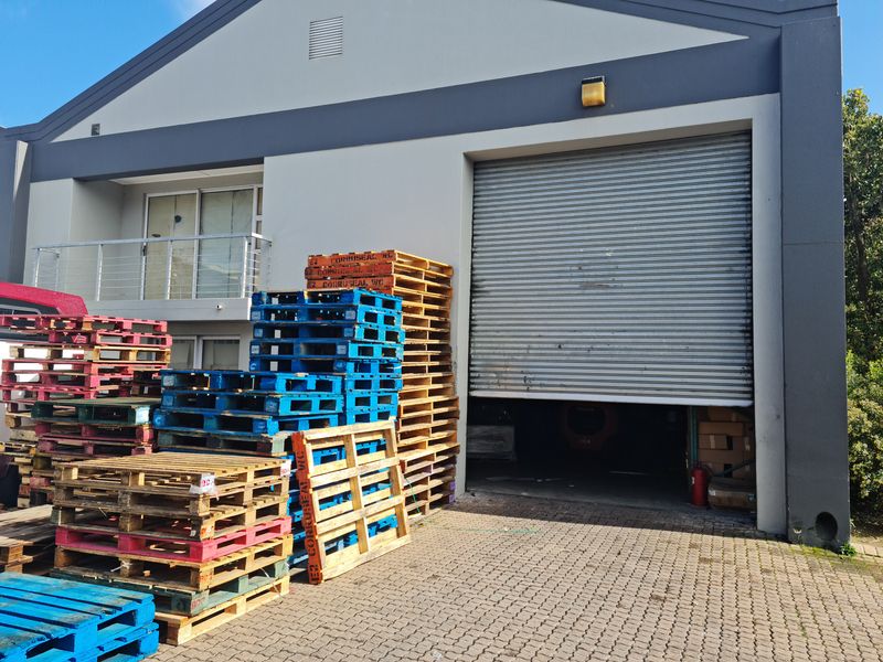 Industrial property exterior featuring a large roller shutter door, paved access area, and an upper-level balcony.