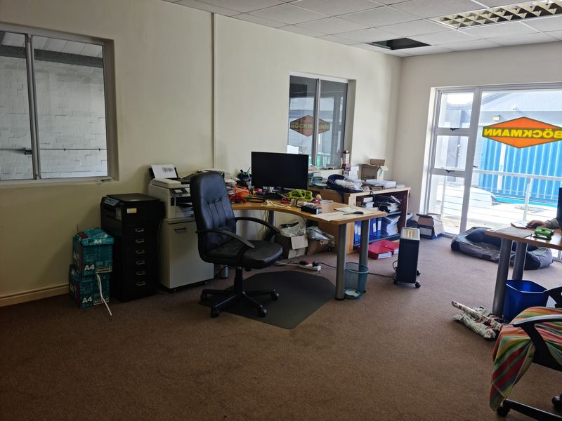 A functional office space featuring carpeted flooring, suspended ceiling tiles, and large aluminium-framed windows providing natural light.