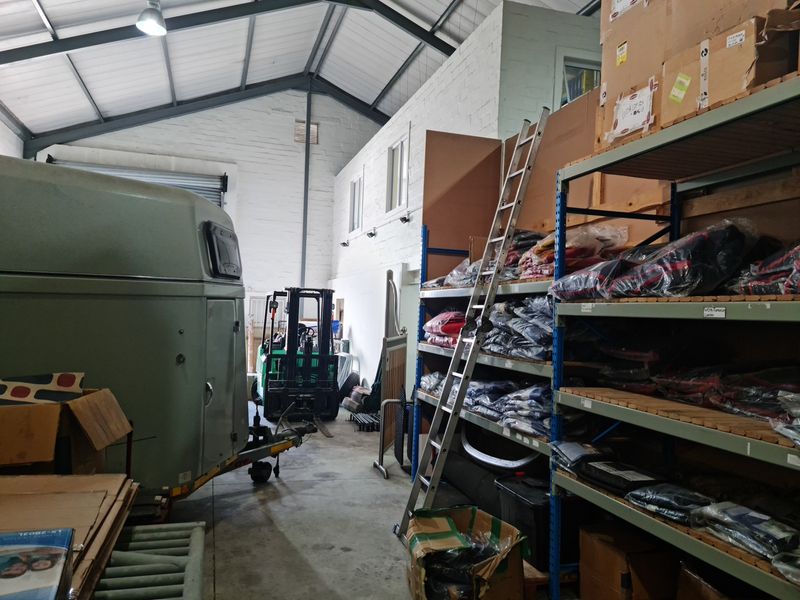 Spacious industrial warehouse or garage area featuring high ceilings with exposed steel trusses, concrete flooring, and painted brick walls, suitable for storage or workshop use.
