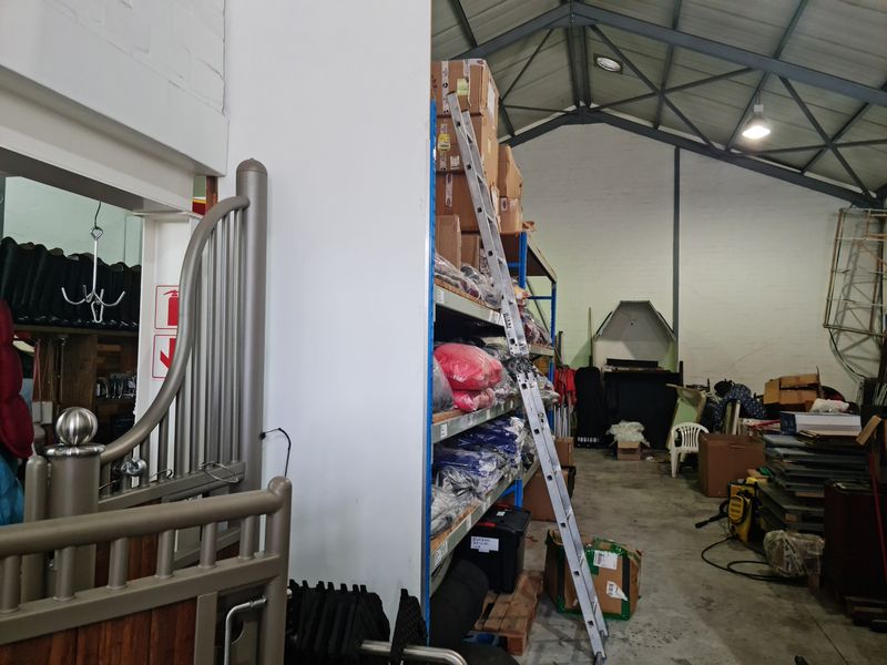 Industrial utility space featuring exposed steel roof trusses, concrete flooring, and built-in industrial shelving units for storage.