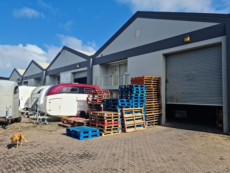 Industrial warehouse unit featuring a large roller shutter door, paved exterior frontage, and a small upper-level balcony.