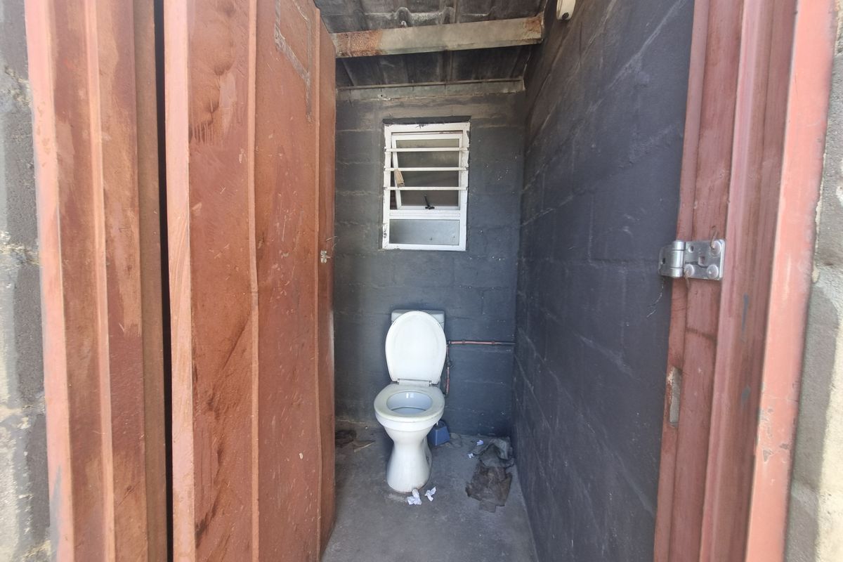 A basic industrial-style outdoor toilet facility featuring exposed concrete block walls, a simple window, and a standard porcelain toilet fixture.