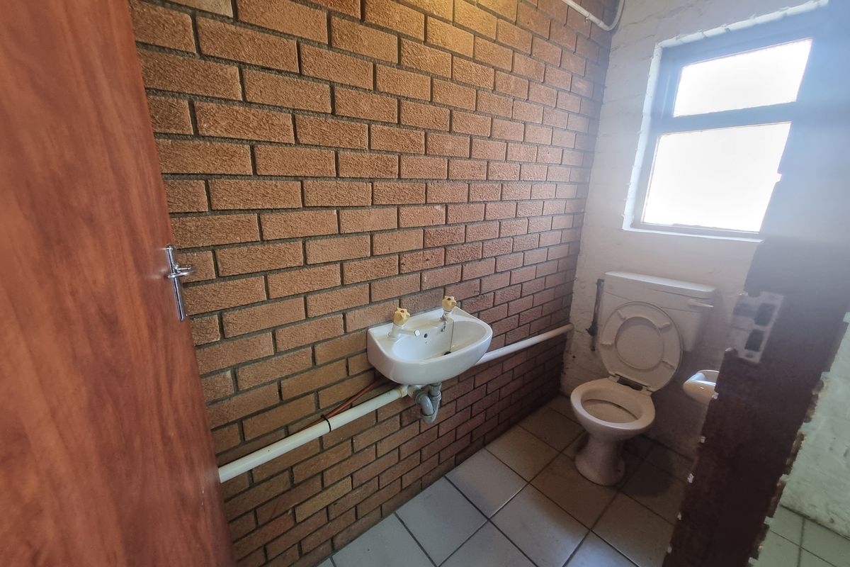 A functional industrial-style restroom featuring exposed brick walls, tiled flooring, a wall-mounted basin, and a standard toilet suite.
