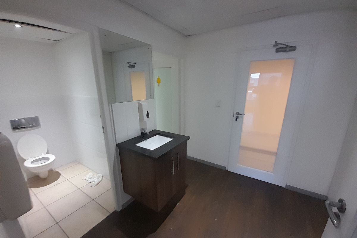 A functional industrial restroom featuring a wall-mounted vanity with a basin, a separate toilet cubicle, and a frosted glass door.