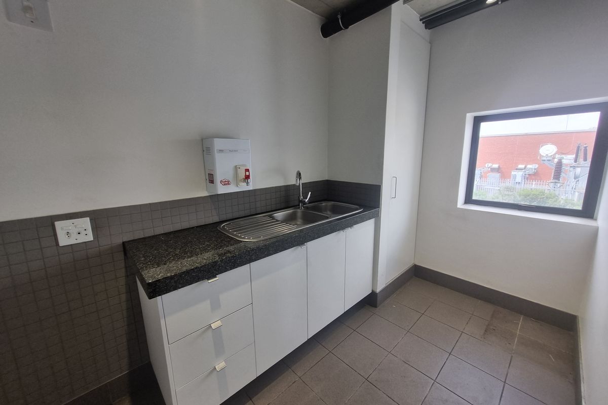 A clean, functional kitchenette area featuring white cabinetry, a dark stone countertop, stainless steel sink, and tiled splashback in an industrial-style space.