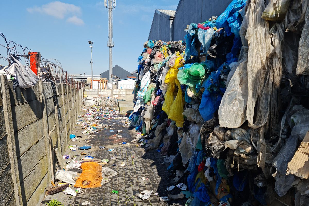 Exterior industrial yard area featuring a perimeter wall with barbed wire and significant accumulation of waste materials.