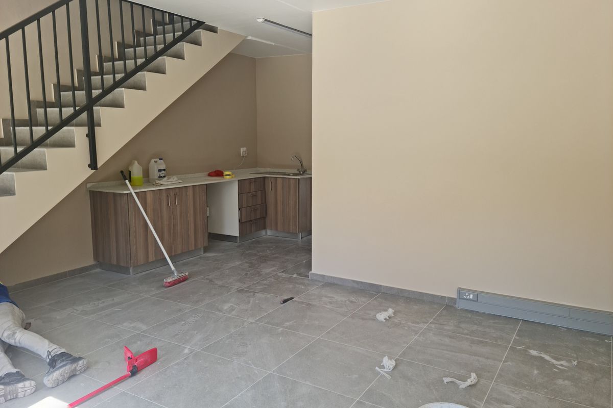 A functional kitchenette area featuring built-in cabinetry, a sink, and tiled flooring, situated beneath an open staircase in an industrial-style space.