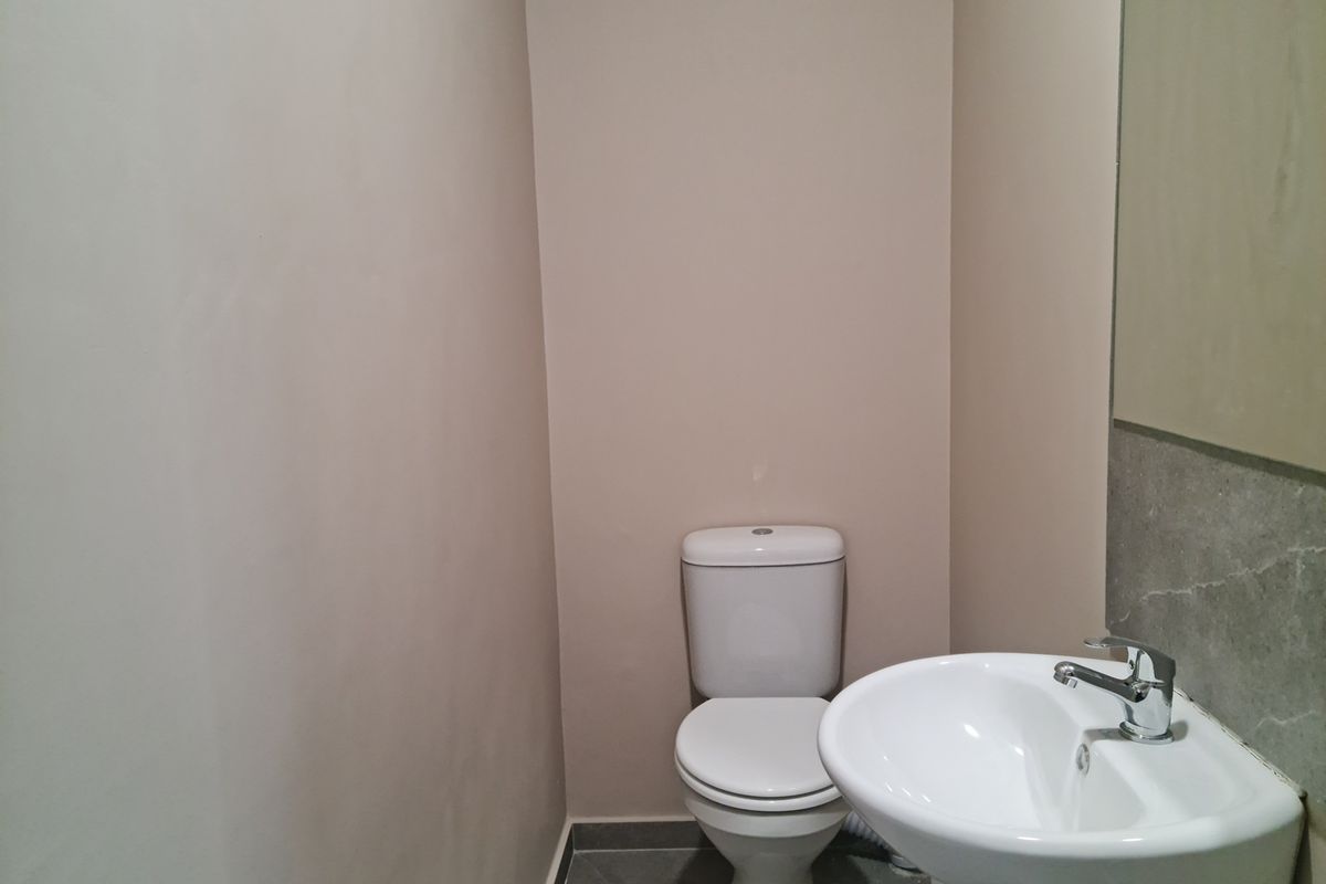 A compact industrial restroom featuring a white pedestal basin, chrome faucet, and a standard white toilet suite.