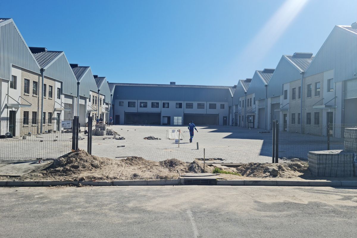 A view of an industrial complex courtyard under construction, featuring multiple warehouse units with metal roofing and paved exterior space.