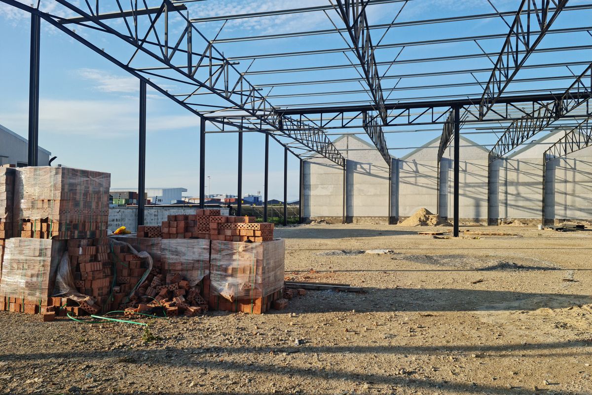 An industrial property under construction featuring an exposed steel portal frame structure and concrete wall panels on a large open site.
