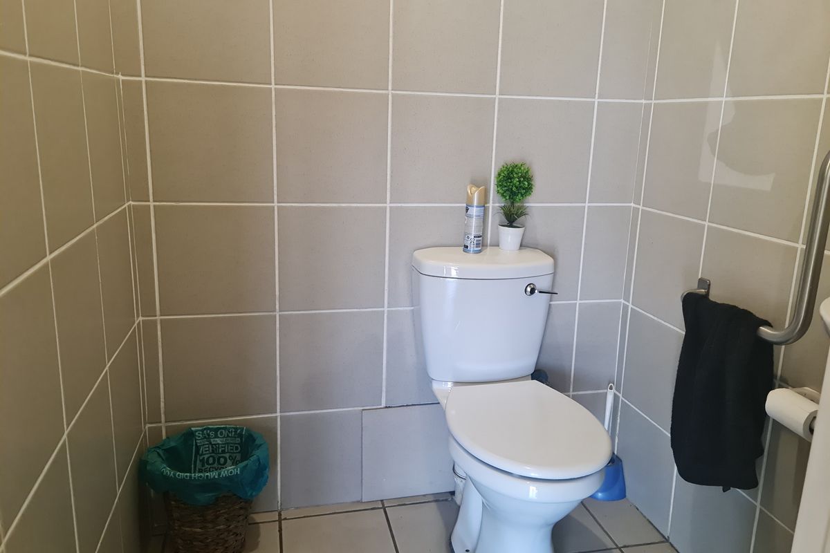 A functional bathroom featuring a standard white toilet, tiled walls, and a grab rail for accessibility.