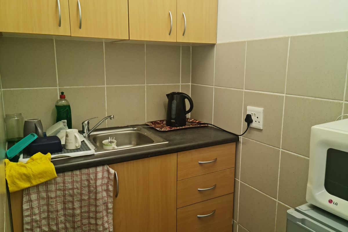 Compact kitchenette featuring laminate cabinetry, a stainless steel sink, and tiled splashback, suitable for a small office or utility space.