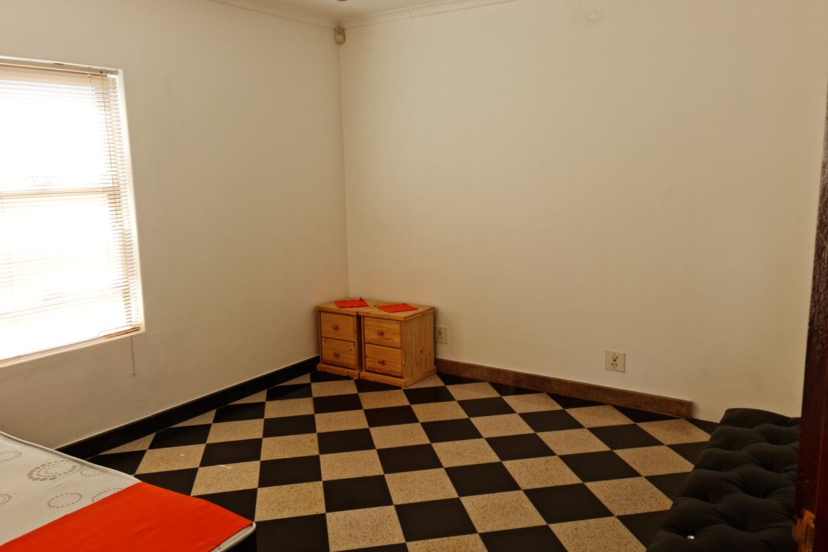 A bedroom featuring a distinctive black and white checkered tiled floor, neutral walls, and a window with fitted blinds.