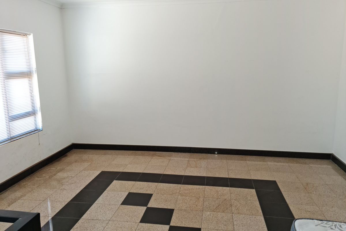 A spacious, empty room featuring polished granite tile flooring with a decorative border and a single window with fitted blinds.