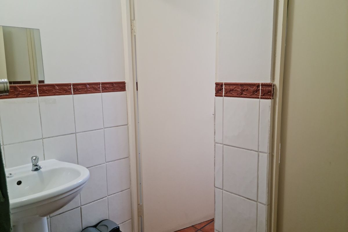A functional bathroom featuring a pedestal sink, white wall tiles with a decorative border, and terracotta floor tiles.