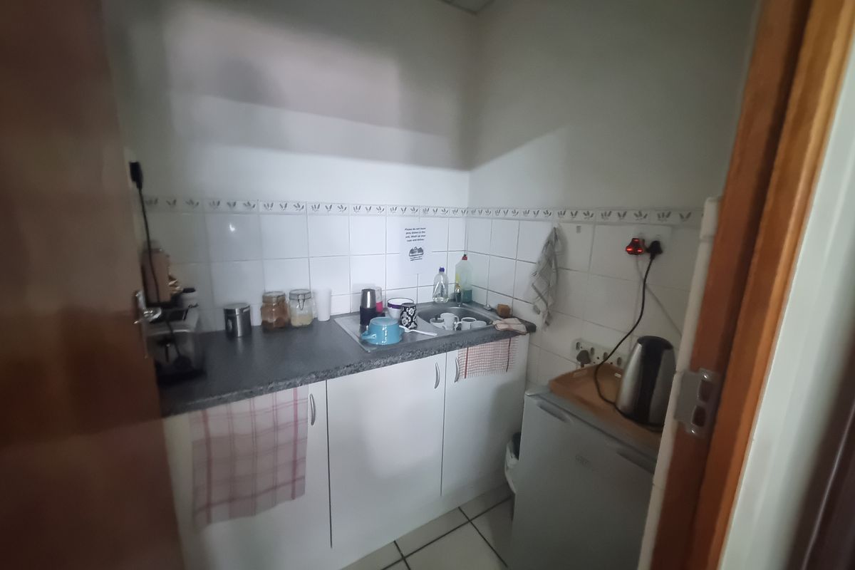 A compact kitchenette featuring built-in cabinetry, a stainless steel sink, and tiled splashback, suitable for a small office or utility space.