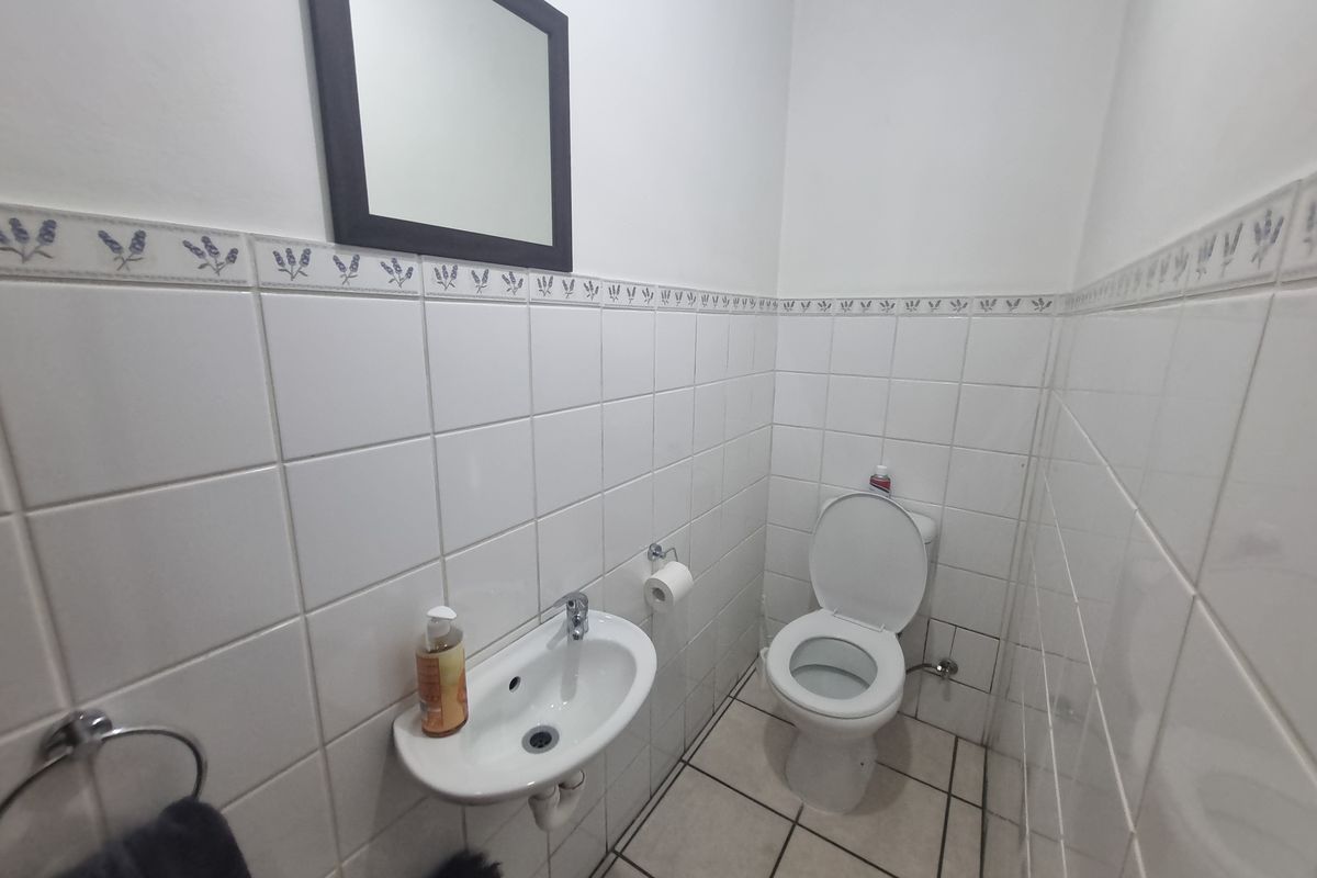 A compact industrial restroom featuring white wall tiles with a decorative border, a wall-mounted basin, and a standard toilet.