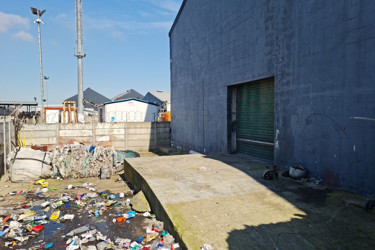 Exterior view of an industrial warehouse featuring a concrete loading bay, roller shutter door, and perimeter walling.
