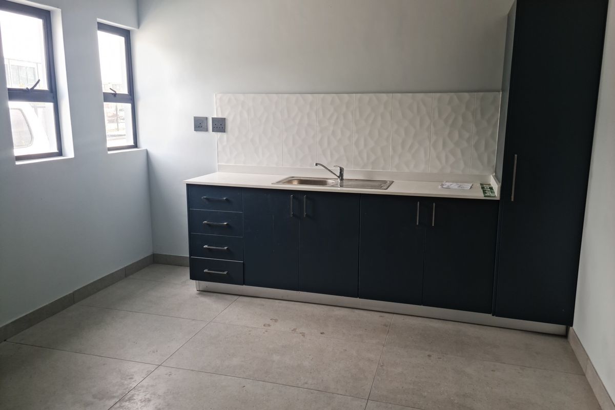 A clean, modern kitchenette featuring dark cabinetry, a stainless steel sink, textured tile backsplash, and large format floor tiles.