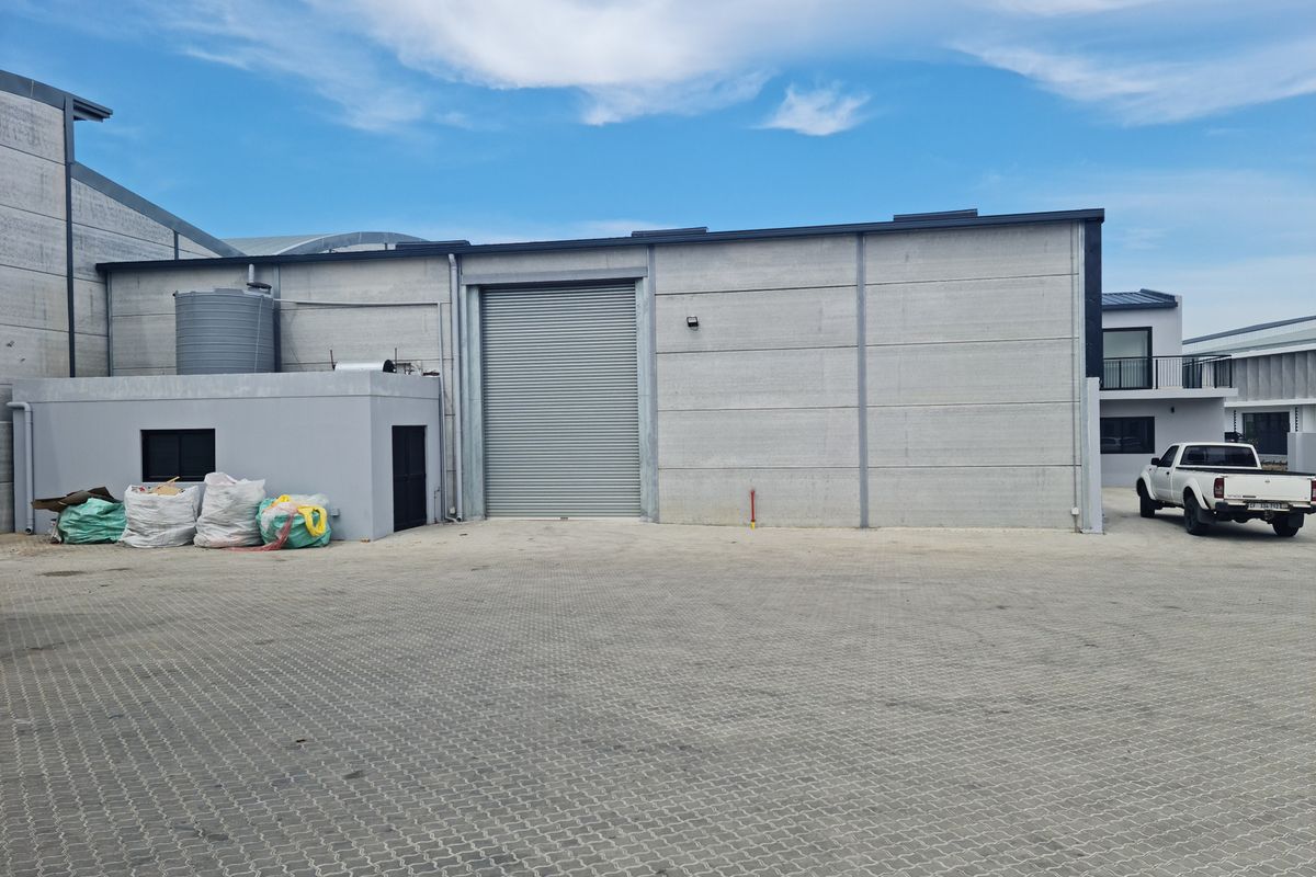 Industrial exterior view featuring a large roller shutter door, concrete panel walls, and paved yard area.