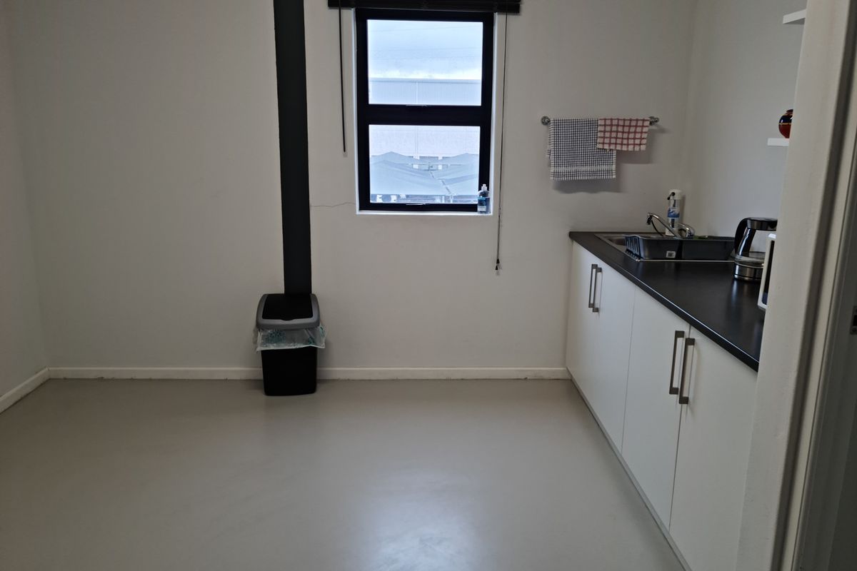 A functional kitchenette area featuring white cabinetry, dark countertops, a stainless steel sink, and a window providing natural light.