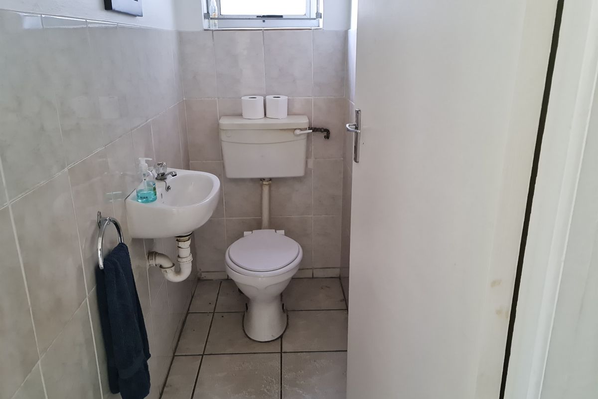 A compact guest bathroom featuring a wall-mounted basin, a standard toilet, and neutral wall and floor tiling.