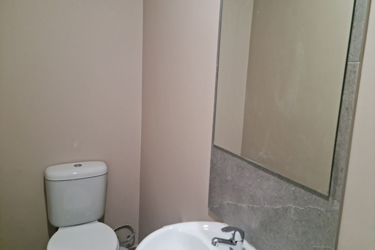 A compact bathroom featuring a white toilet, a pedestal sink with a chrome faucet, and a wall-mounted mirror with stone-look tile backsplash.