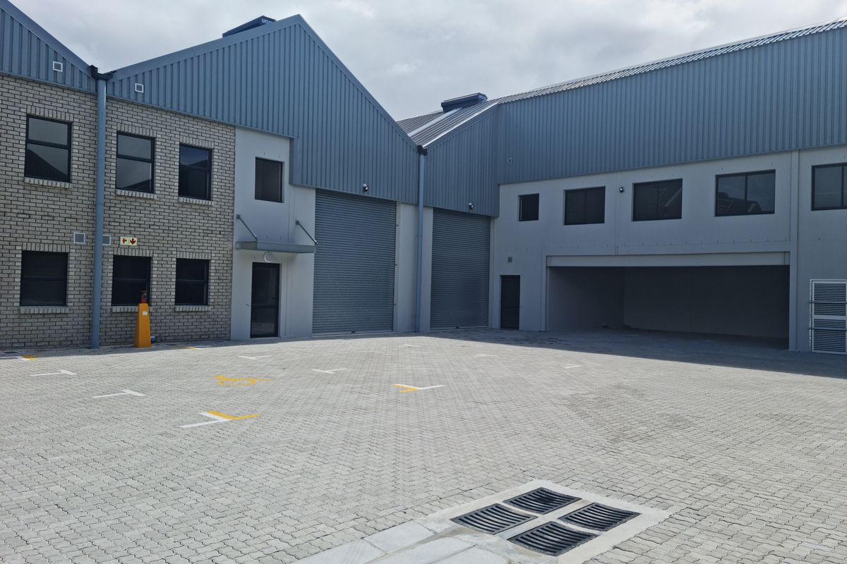 Modern industrial warehouse complex featuring paved yard space, roller shutter doors, and multi-level office or storage windows.