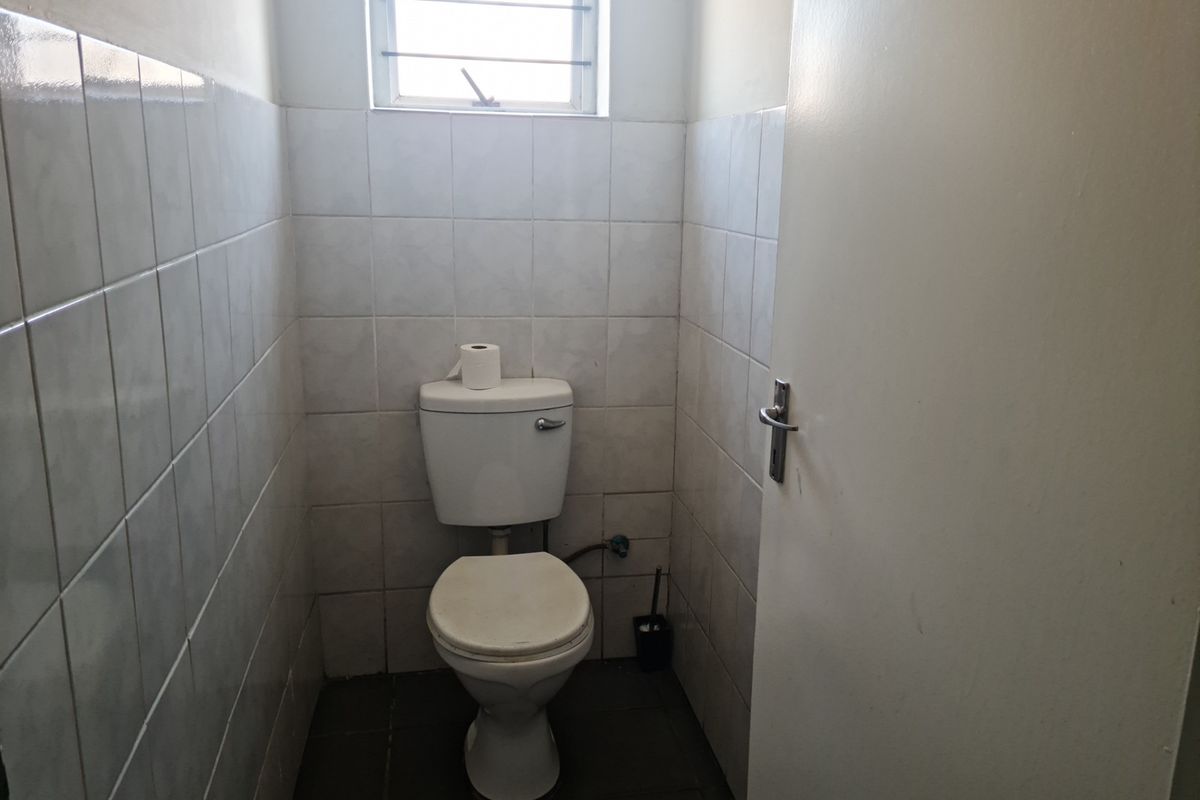 A compact industrial restroom featuring tiled walls, a standard toilet, and a small high-level window for ventilation.