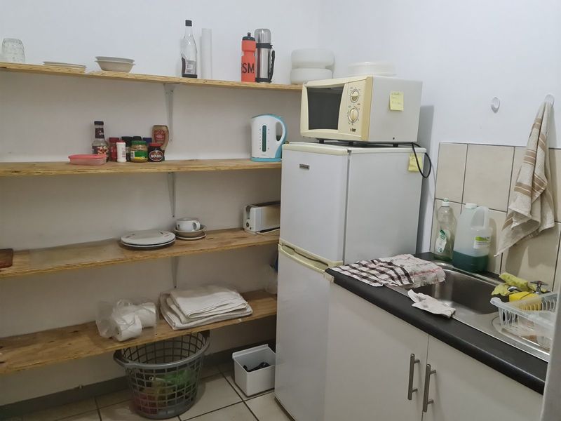 A functional scullery area featuring open timber shelving, a stainless steel sink, tiled splashback, and basic base cabinetry for storage.