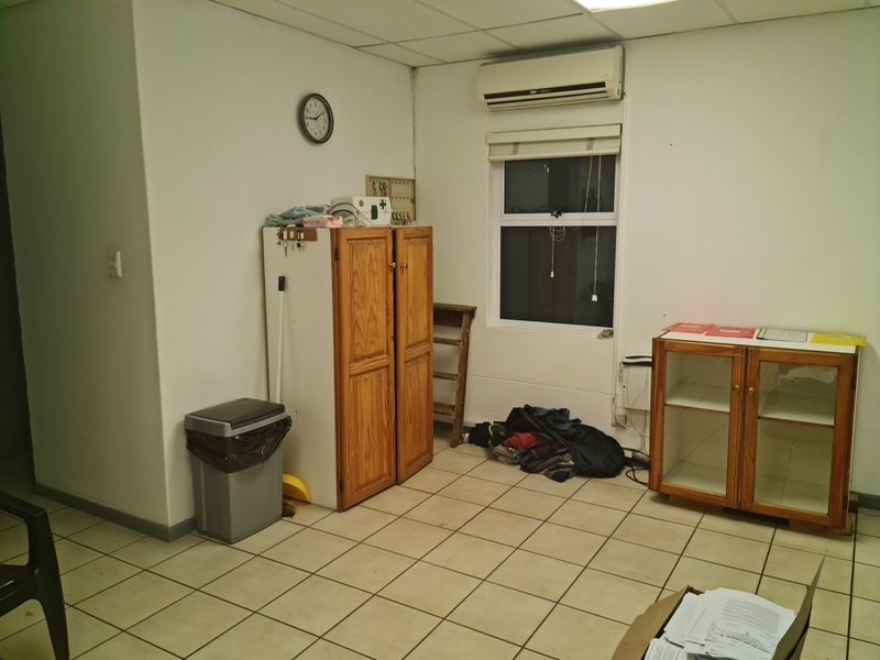 A functional office space featuring tiled flooring, a drop ceiling, and a wall-mounted air conditioning unit, providing a practical workspace environment.