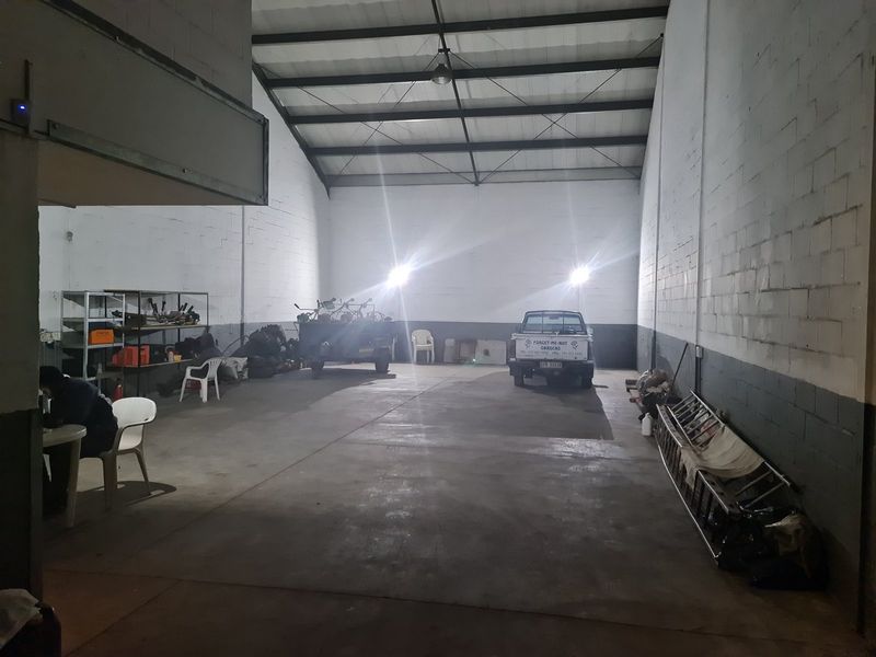 Spacious industrial garage or warehouse unit featuring high ceilings with exposed steel trusses, concrete flooring, and durable blockwork walls.