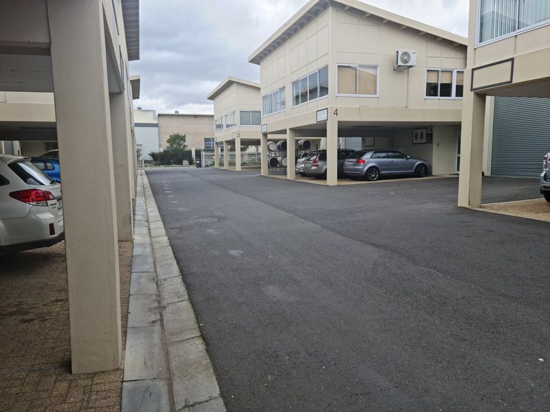 View of an industrial complex featuring multiple units with covered parking bays, asphalt driveway, and concrete structural pillars.