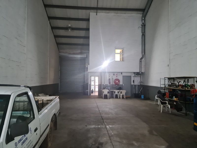 Spacious industrial utility area featuring high ceilings with exposed steel trusses, a large roller shutter door, and durable concrete flooring.