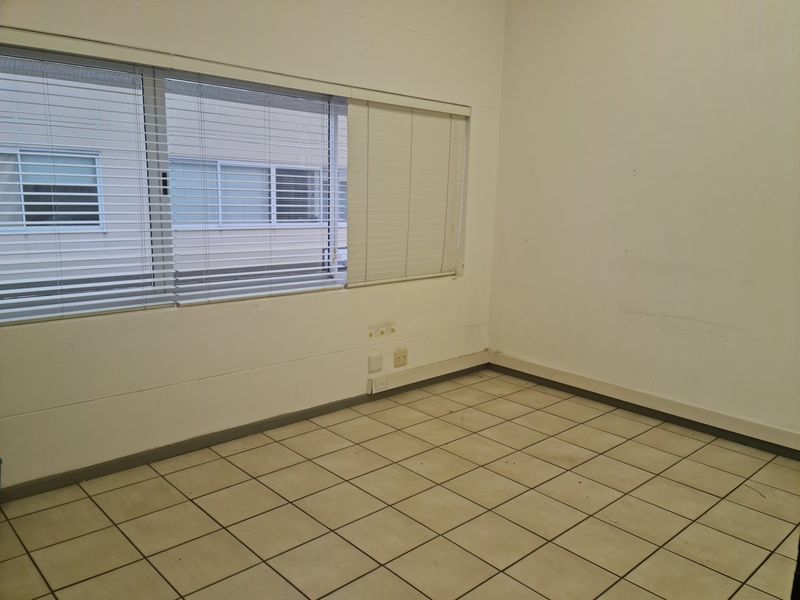 An empty, functional office space featuring tiled flooring, horizontal window blinds, and wall-mounted electrical outlets, ready for customization.