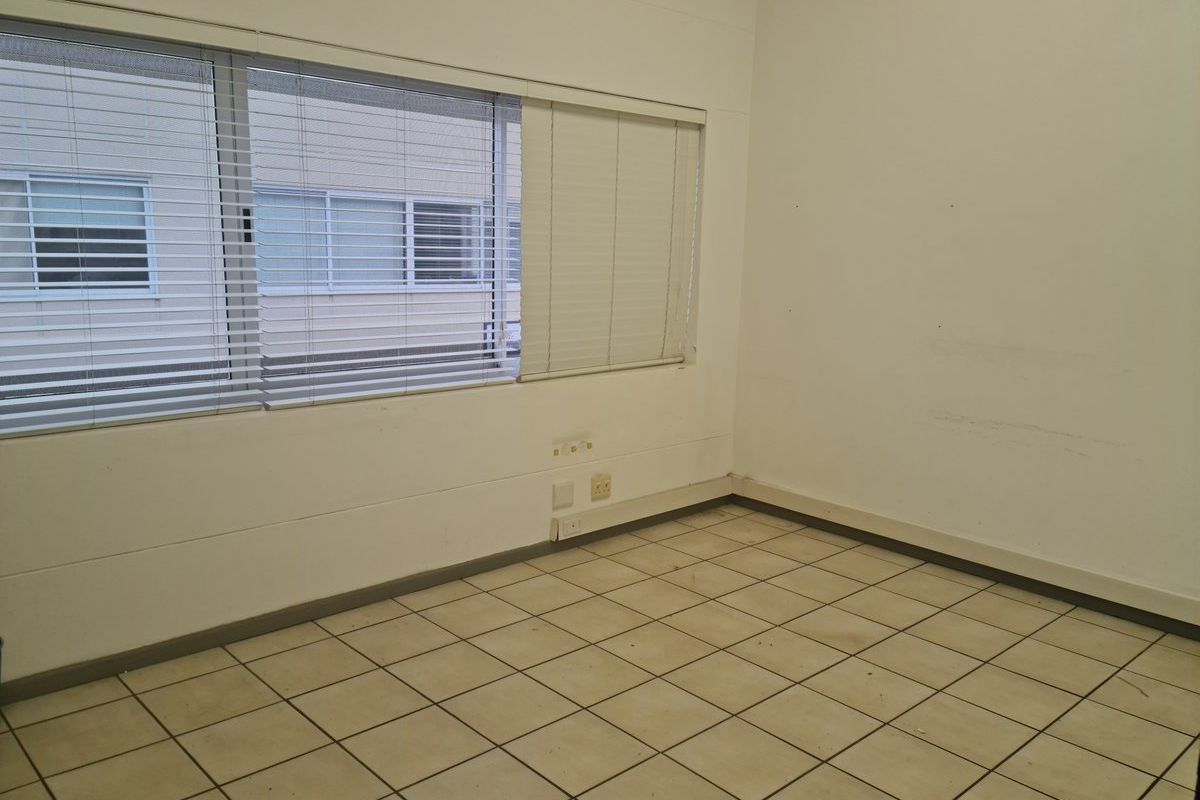 An empty, functional office space featuring tiled flooring, horizontal window blinds, and wall-mounted electrical outlets, ready for customization.