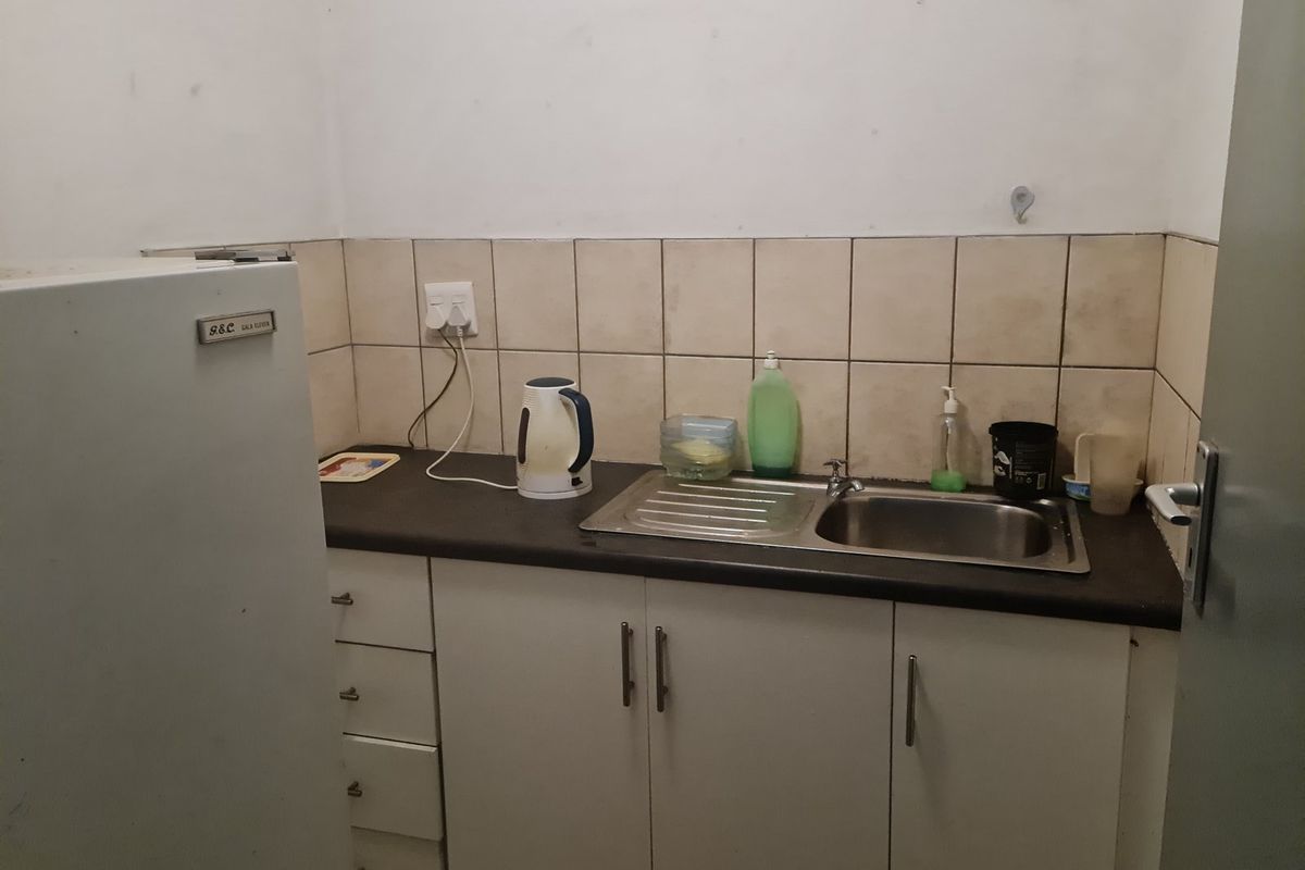 A compact kitchenette featuring a stainless steel sink, laminate countertop, and tiled splashback, showing signs of wear and requiring cosmetic updates.