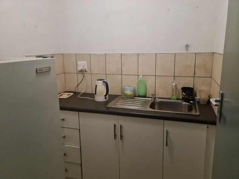 A compact kitchenette featuring a stainless steel sink, laminate countertop, and tiled splashback, showing signs of wear and requiring cosmetic updates.