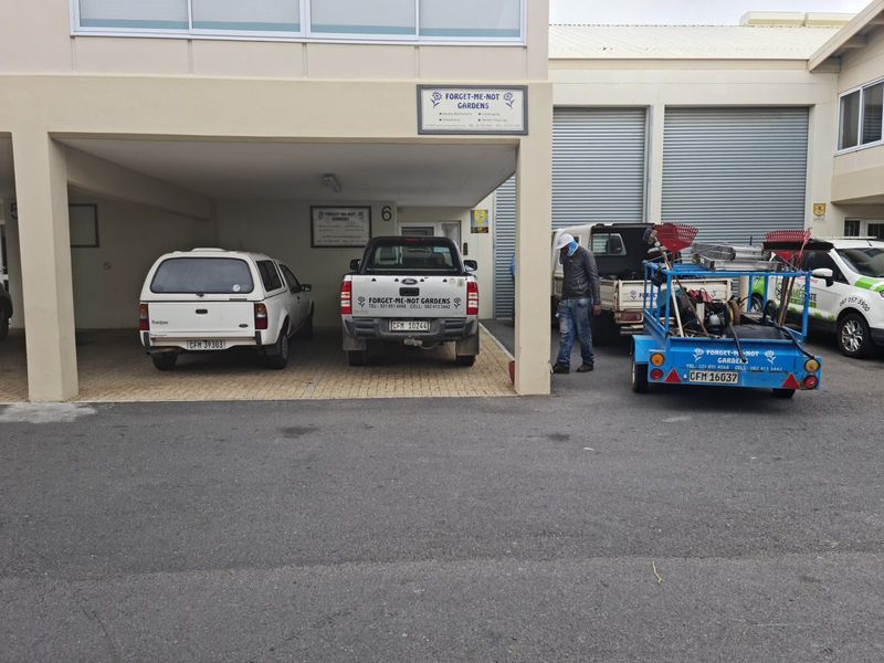 Industrial property exterior featuring a covered parking area and multiple roller shutter doors for vehicle access.