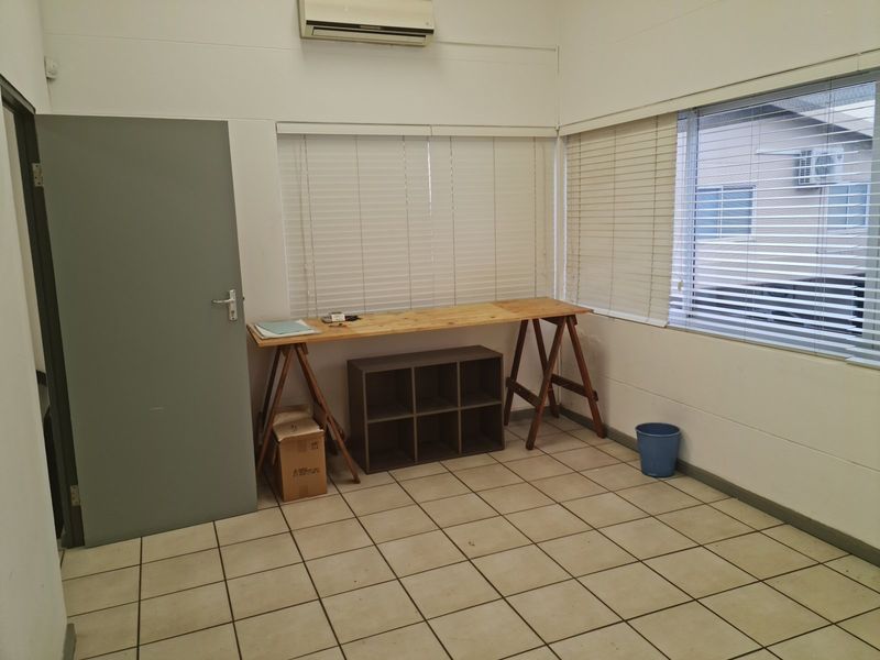 A functional office space featuring tiled flooring, split-system air conditioning, and large windows with fitted venetian blinds.