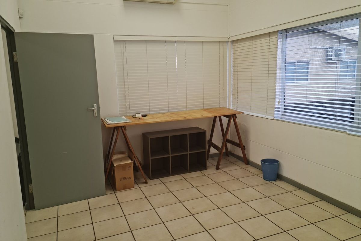 A functional office space featuring tiled flooring, split-system air conditioning, and large windows with fitted venetian blinds.