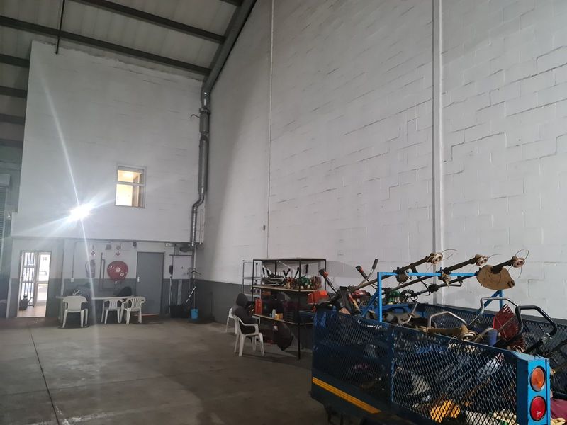 Spacious industrial utility area featuring high ceilings with exposed steel trusses, durable concrete flooring, and painted masonry walls.