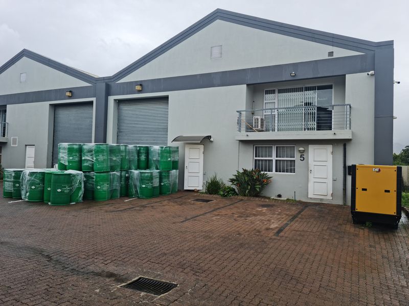 Industrial unit exterior featuring roller shutter doors, a paved driveway, and an upper-level balcony with security gates.