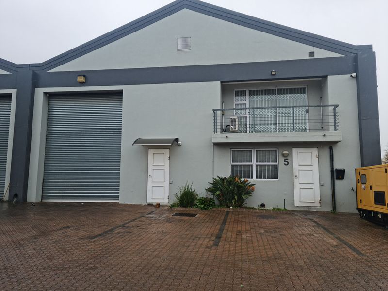 Front elevation of an industrial unit featuring a large roller shutter door, a balcony, and paved parking area.