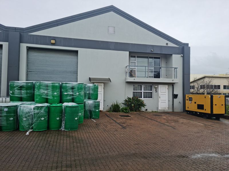 Front elevation of an industrial unit featuring a roller shutter door, paved forecourt, and a small balcony, with a backup generator on-site.
