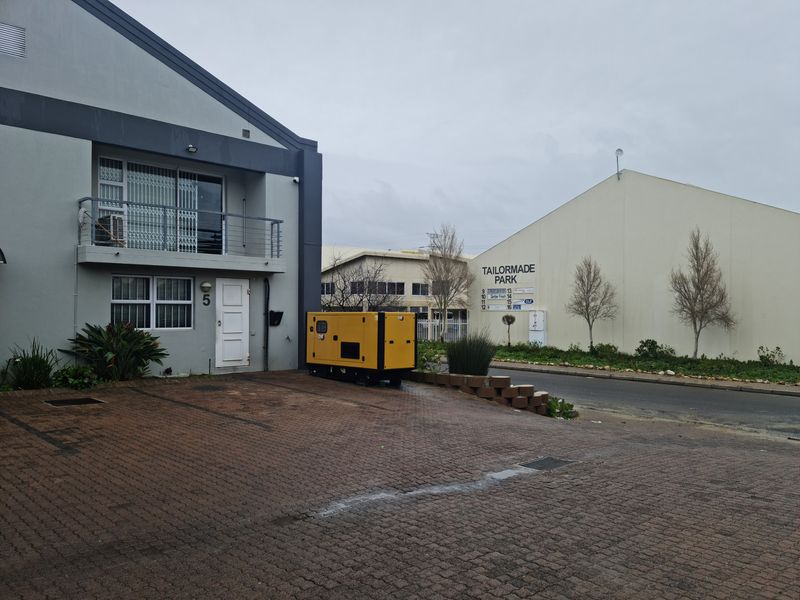 Front exterior view of an industrial unit featuring a paved driveway, balcony, and dedicated backup generator within a business park setting.